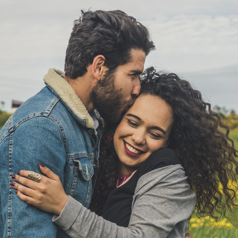 Couple in field of flowers. Man is kissing woman on cheek.