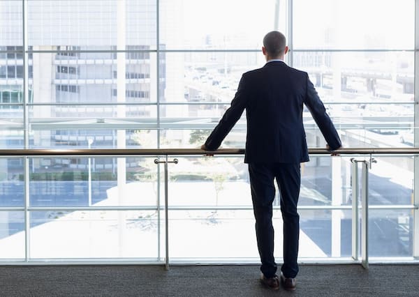 A business man stands with his hands on a railing while facing a large window, illustrating that Susan Gonzales provides therapy for men.