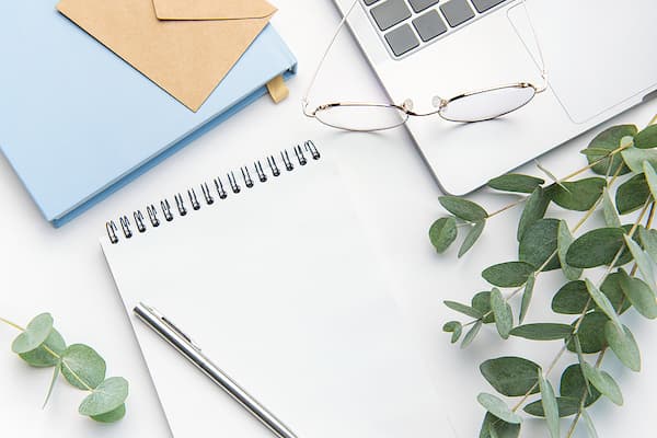 Modern white office desk table with a laptop, notebooks, pen, and eye glasses.