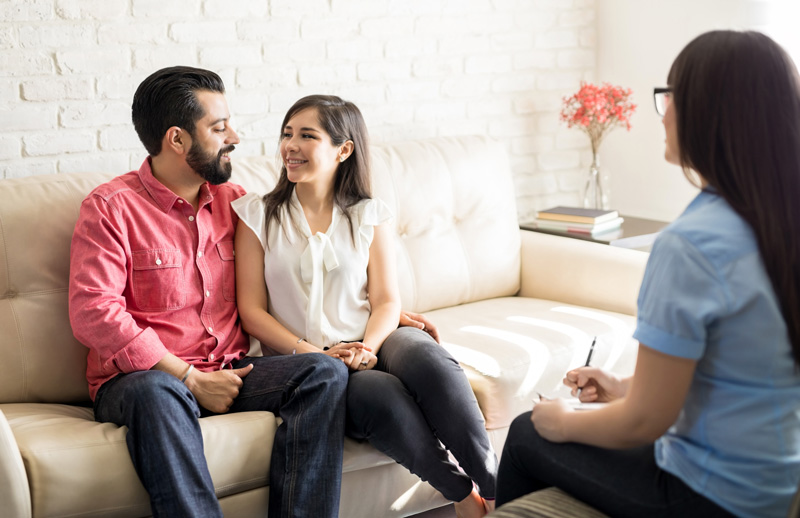 neurodivergent couple in counseling session sitting on couch looking at each other. Counselor is sitting across from couple